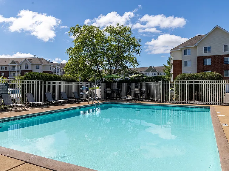 Inviting outdoor pool with lounge chairs, surrounded by a well-maintained fence and lush greenery, perfect for relaxation and leisure in a modern apartment community.