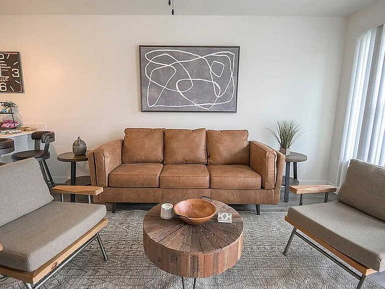 Chic living room featuring a stylish brown leather sofa, modern artwork, and rustic wooden coffee table, creating a cozy and elegant ambiance.