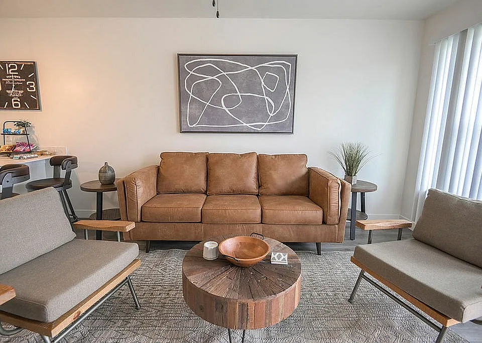 Chic living room featuring a stylish brown leather sofa, modern artwork, and rustic wooden coffee table, creating a cozy and elegant ambiance.