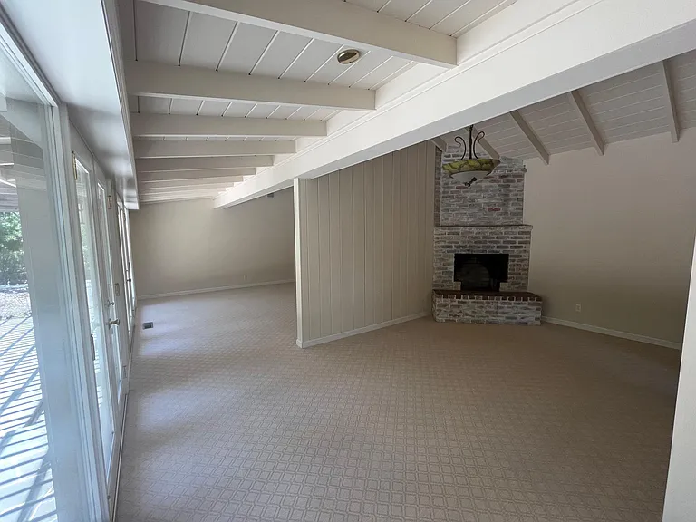 Bright, airy living room features high vaulted ceiling, two wood burning fireplaces, plush carpeting and floor-to-ceiling glass panels and patio doors that flows to a relaxing backyard with a trellis patio cover surrounded by mature trees.