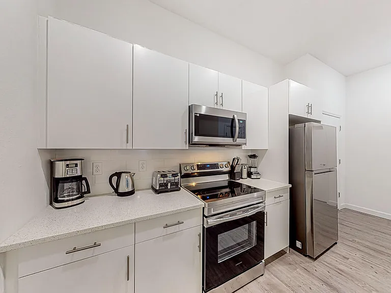 Efficient kitchen with ample cabinetry, solid-surface counters, and stainless-steel appliances including microwave and range.