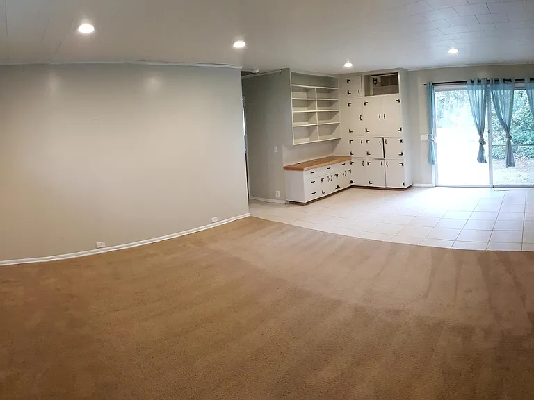 In the back living room an oversized sliding glass door out to back yard patio, tile flooring, built in cabinetry, and new carpet.