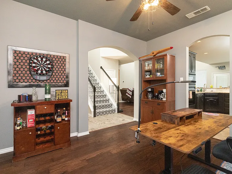 Dedicated office space with a desk, ergonomic chair, and coffee cabinet. Brick accent wall and ceiling fan create a cozy and inspiring work environment.