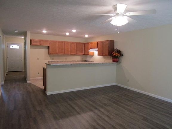 Craftsman style entry door (and adjacent garage entry to inside) opens to a dark brown/gray vinyl tile foyer with cream colored walls and white trim. Brown laminate flooring in the living room, which has a white paddled ceiling fan with four covered ligh