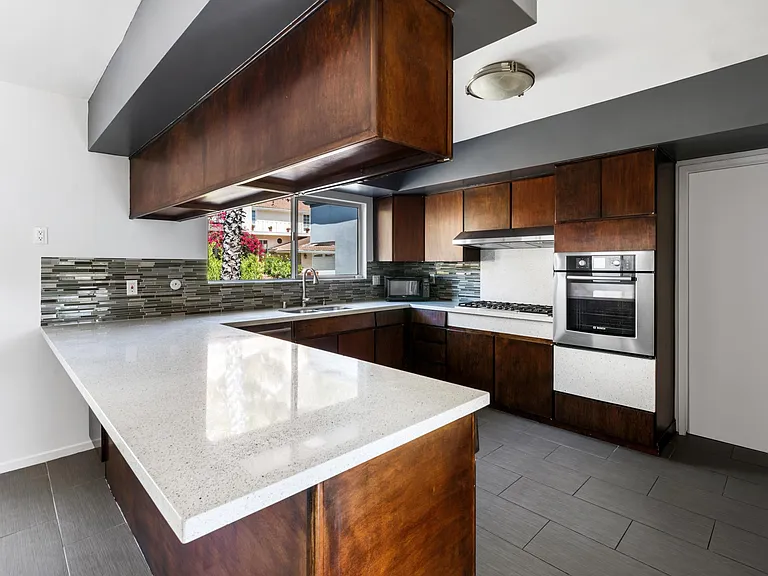 Caesarstone with recycled glass counters, sliding shelves in cabinets, Bosch oven, dishwasher and stove with overhead fan and light. Ample cabinets, including utility cover for central vacuum. Pocket door leads to den. Patio door leads to tea garden.