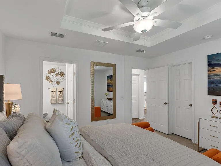 Spacious furnished bedroom with tray ceiling, ceiling fan, and easy access to nearby bath and closet storage.
