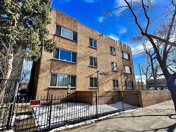 Charming brick apartment building with large windows, surrounded by trees, offering a cozy and inviting urban living experience.