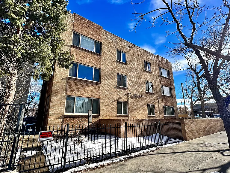 Charming brick apartment building with large windows, surrounded by trees, offering a cozy and inviting urban living experience.