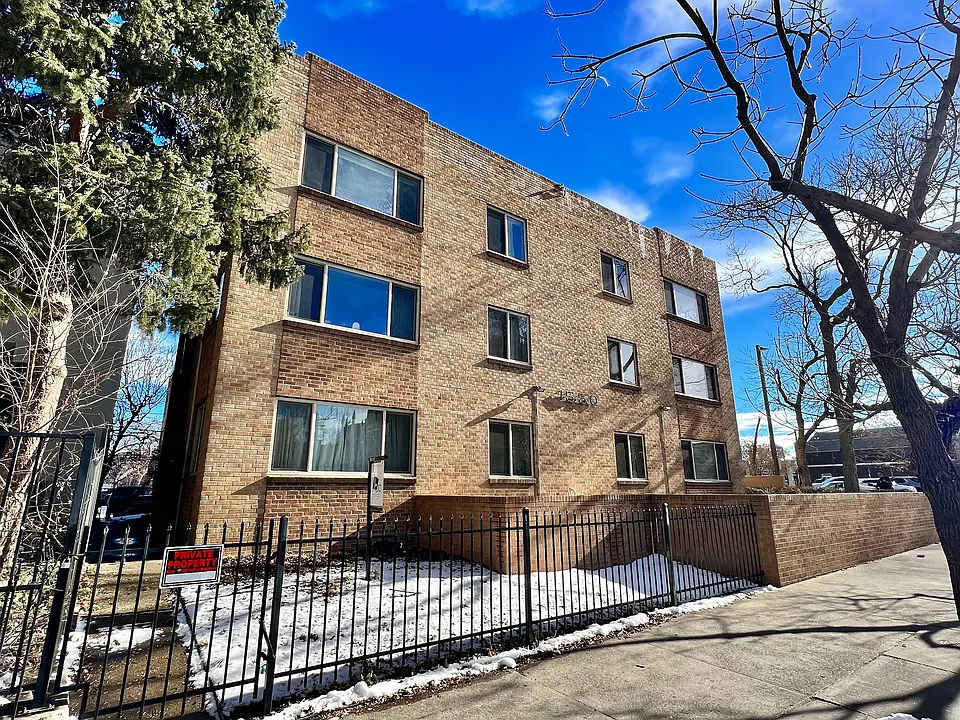 Charming brick apartment building with large windows, surrounded by trees, offering a cozy and inviting urban living experience.