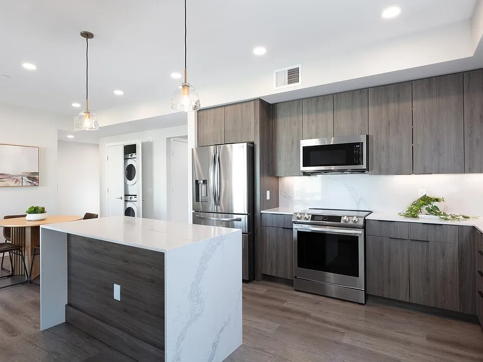 Signature Collection Kitchen with wood cabinetry, marbled quartz countertop and backsplash, upgraded stainless steel appliances, and hard surface flooring