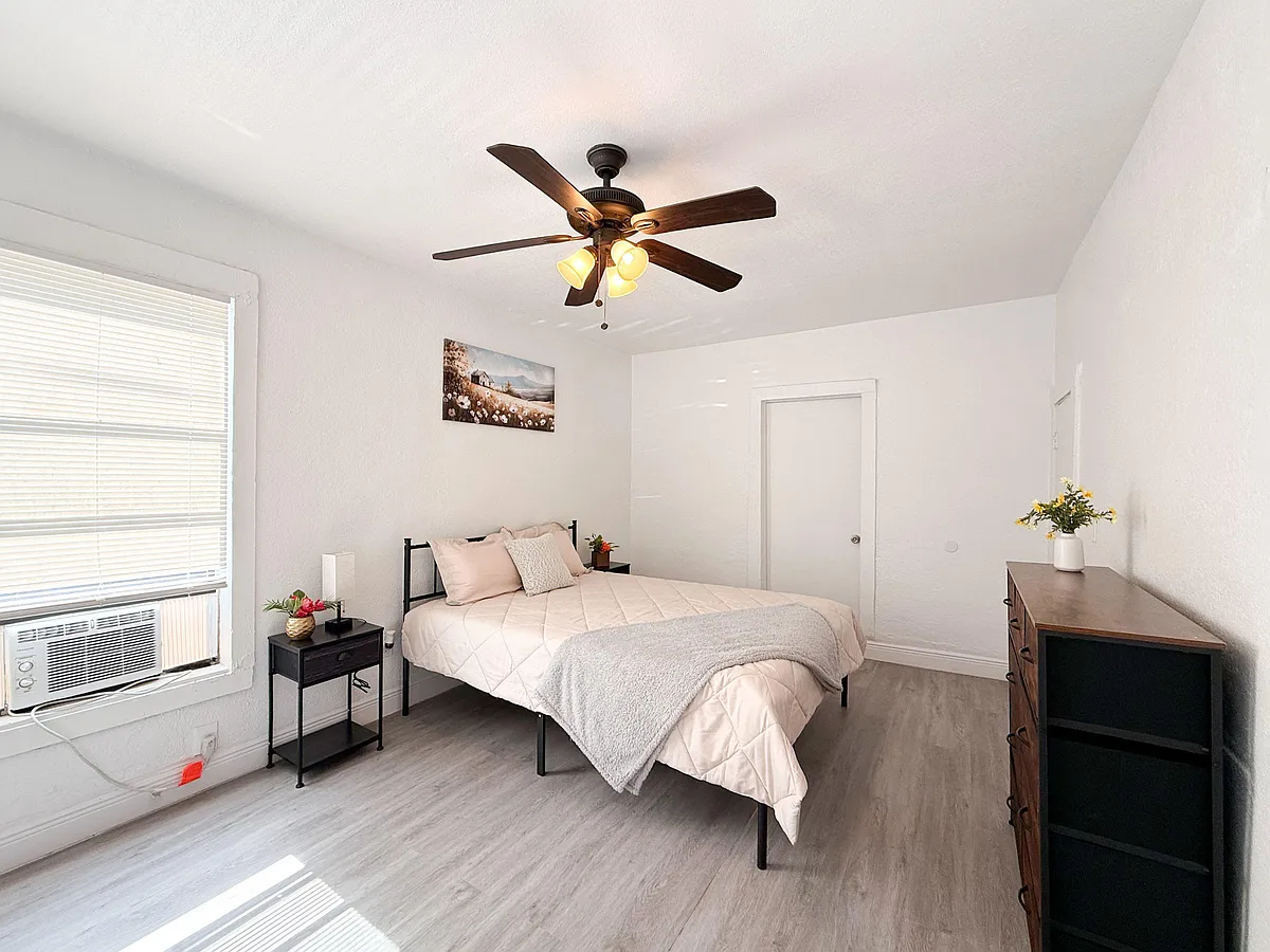 Furnished bedroom with a full-size bed, dresser, and nightstand, plus a large window and ceiling fan with light. - E Kentucky Ave