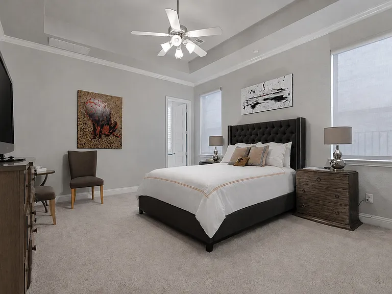 This expansive downstairs primary suite serves as a serene private retreat, showcasing an elegant tray ceiling with double crown molding, plush carpeting, and bright windows that fill the space with soft, natural light.