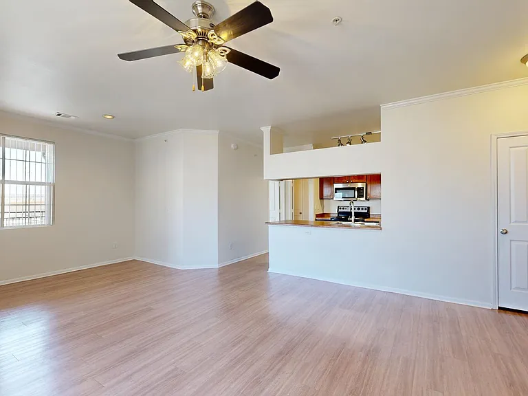 Apartment kitchen with stainless steel appliances, dining and living room with plush carpet flooring.