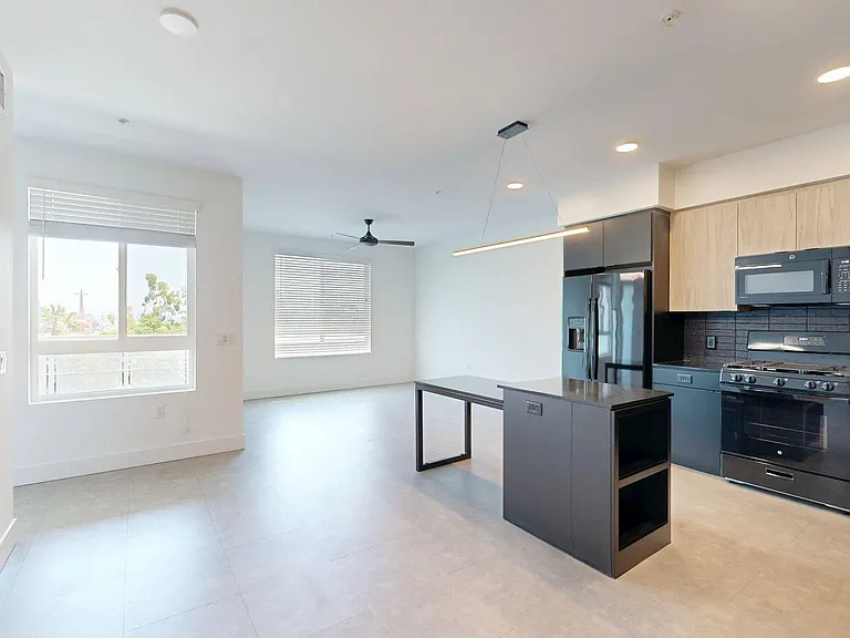 Apartment kitchen with black appliances, dining, and living room with wood style floor.