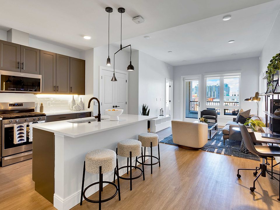 Modern open-plan kitchen and living area with sleek cabinetry, a chic island with bar stools, and large windows offering vibrant city views.