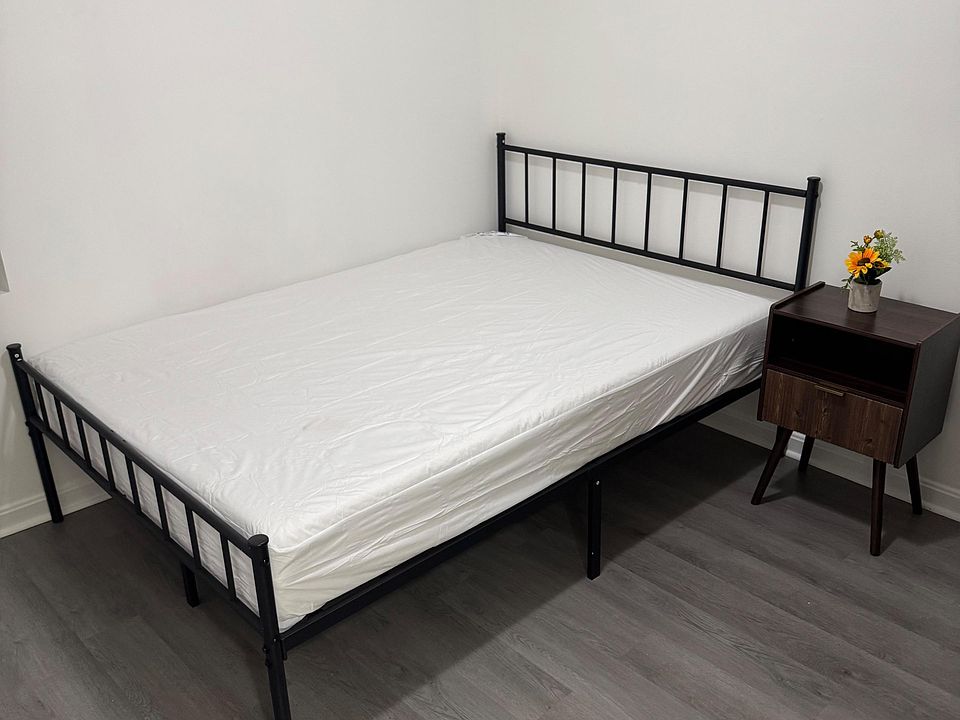 Furnished bedroom with a metal bed frame, nightstand, and durable flooring, offering a simple setup for restful living.