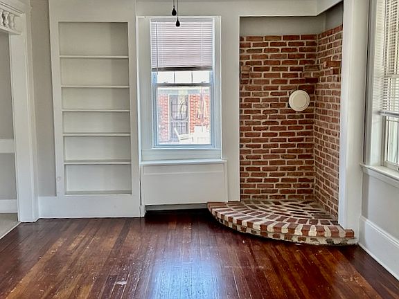 Living room with hardwood floors, built in and accent brick corner - perfect for display, decor or electric stove.