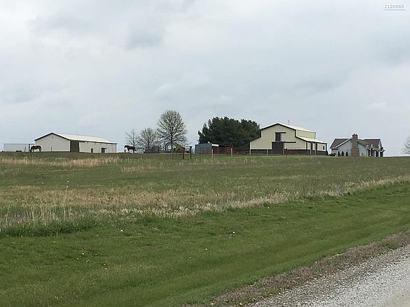 View of the farm from the west drive in.  You can see the row of 15 or more tall evergreen trees that are behind the house.  Barn 1, Barn 2, and the Riding Arena.