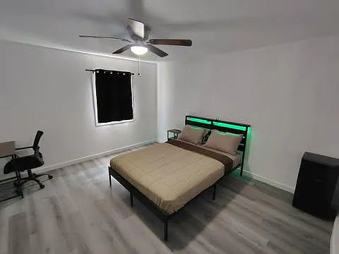 Spacious bedroom with a ceiling fan, large bed, and room for a desk setupideal for work and rest.