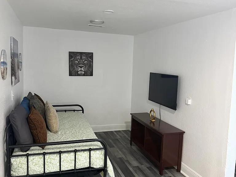 Furnished bedroom with a twin bed, wall-mounted TV, and dresser, plus durable wood-look flooring for easy upkeep.