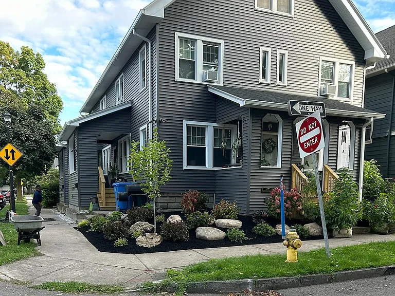 Front corner of building after recent landscaping was completed. Additional landscaping has been installed, including a row of blue perennial flowers between the sidewalk and the building in front of the available unit.