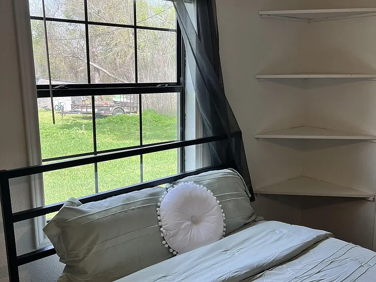 Furnished bedroom with a large window for outdoor views, a twin bed setup, and convenient corner wall shelving.