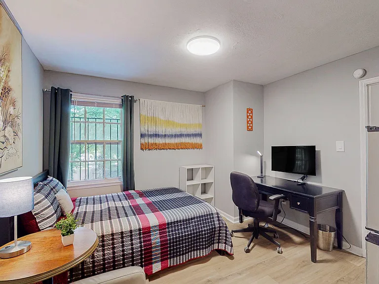 Furnished bedroom with a work desk, TV, and window with curtains for added privacy and natural light.