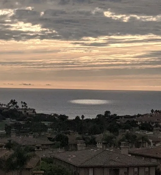 Cloud-veiled sun glows on the Pacific from elevated balcony.