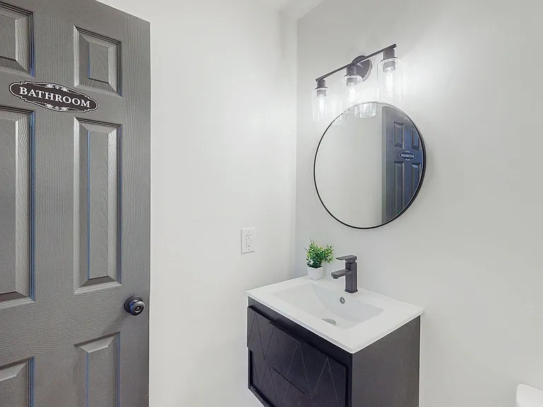 Updated bathroom vanity area with an undermount sink, matte black faucet, round mirror, and modern overhead lighting.