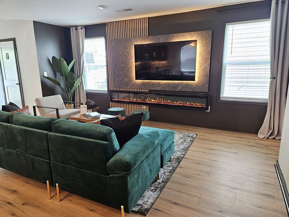 Step into elegance with this beautifully designed living space featuring a plush green sectional, modern accents, and a sleek flickering fireplace. The warm tones and natural light create a inviting atmosphere for relaxation and togetherness.