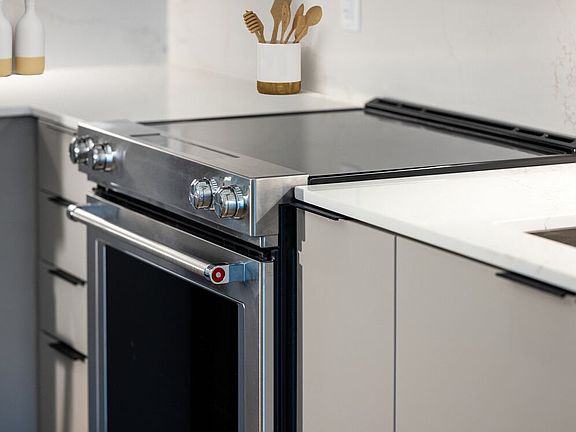 Signature Collection kitchen with light grey cabinetry, electric stove, and marbled quartz countertops and backsplash