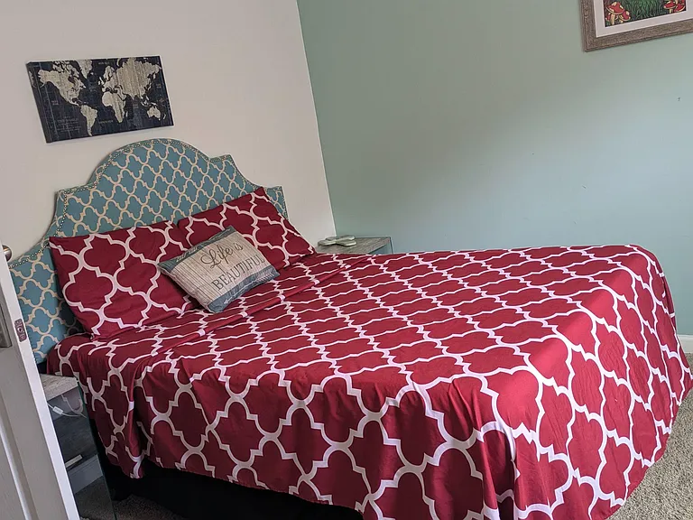 Furnished bedroom with a full/queen bed, patterned upholstered headboard, nightstand, and carpeted flooring.
