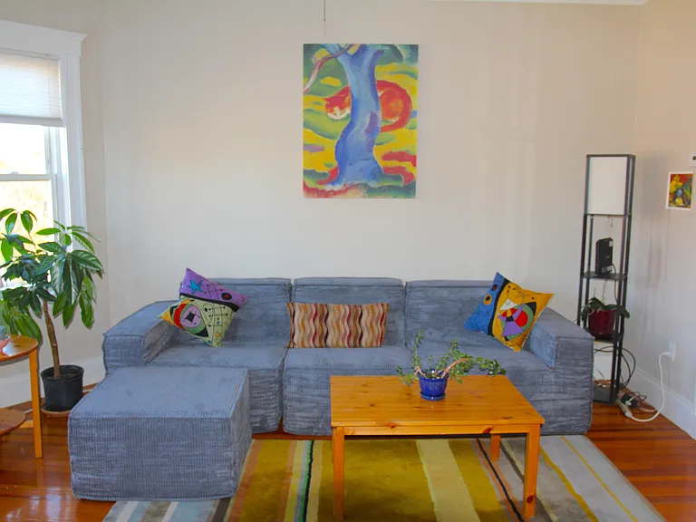 Sunny, cosy living room updated 2025 with powerful window-mounted cooling & new couch. Overlooks ball park and features bay windows, & polished wooden floors.
