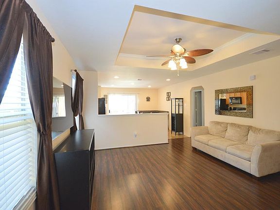 The entry leads to the spacious Living Room featuring wood floors, a high ceiling, a ceiling fan & neutral paint.