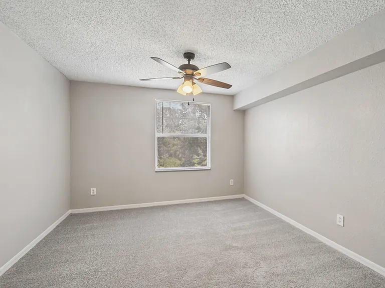 Carpeted bedroom with large window, ceiling fan, and neutral finishes in a 1-bedroom apartment at Gregory Cove in Jacksonville, FL.