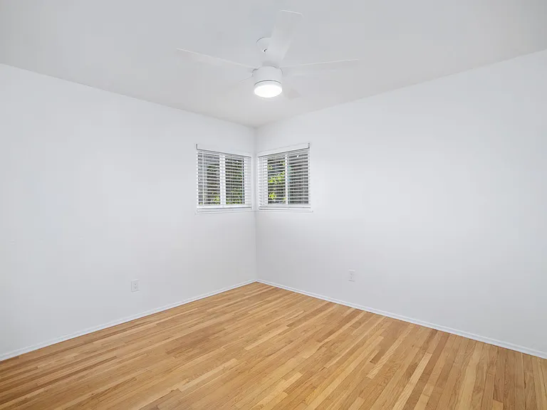 Bedroom #1 showcases abundant natural light and boasts gorgeous hardwood floors alongside a sleek, newly installed ceiling fan.