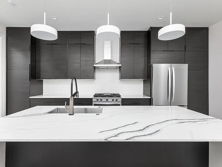 Kitchen with cabinetry to ceiling, designer pendants, stainless steel appliances, and waterfall island