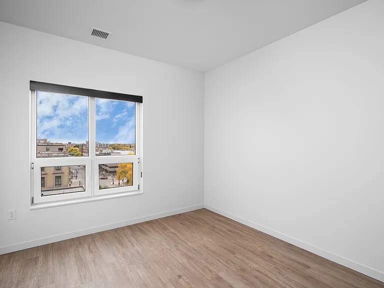 Bright bedroom with large window and stylish wood flooring offering picturesque city views. Bright bedroom with large window and stylish wood flooring offering picturesque city views.