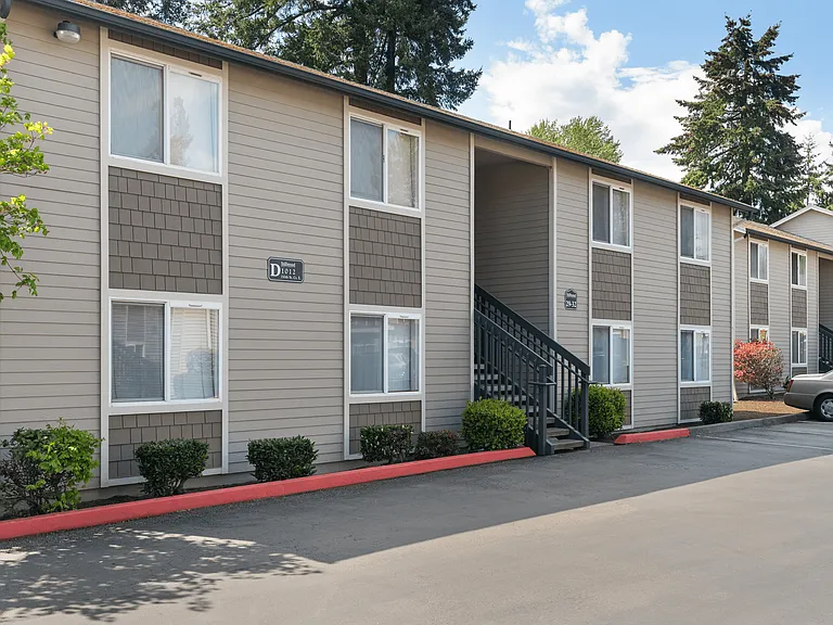 Appealing apartment building with carport parking, landscaped greenery, and a clear blue sky backdrop.