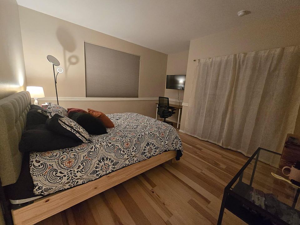 Furnished bedroom with a queen bed, dedicated desk area, wall-mounted TV, and wood-style flooring for easy upkeep.