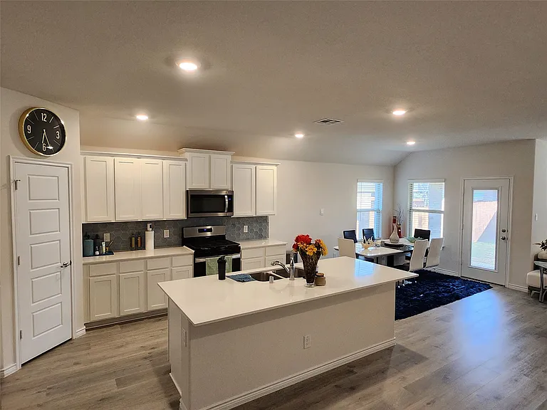 Open-concept kitchen featuring an island with an integrated sink, white cabinetry, stainless steel appliances, and a tiled backsplash