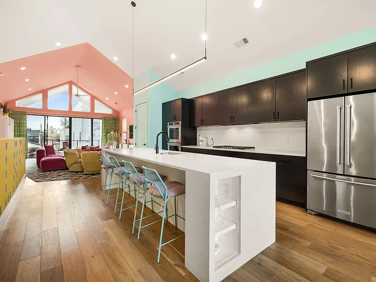 Open-concept kitchen featuring a waterfall island with integrated beverage cooler, stainless steel appliances, dark wood-finish cabinetry, and wood-finish flooring