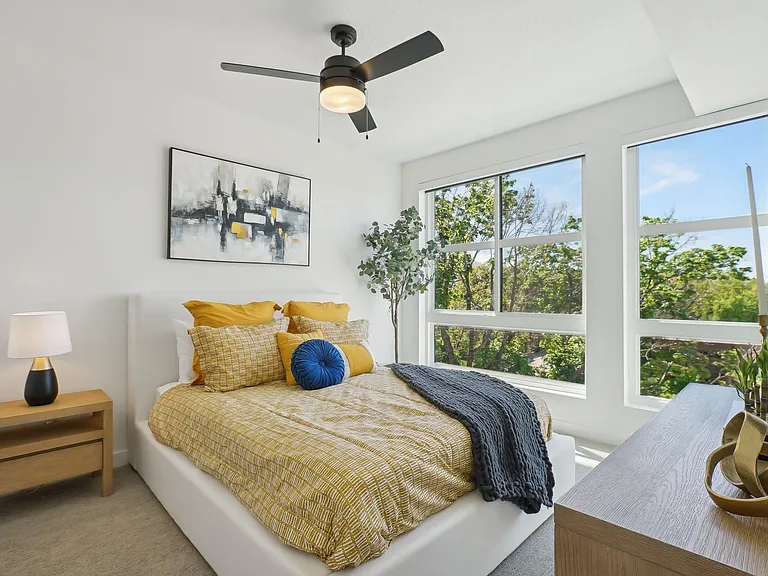 Liberty Duet Apartments, Salt Lake City, Utah; A bedroom with a bed, a ceiling fan, and a window overlooking a forest.