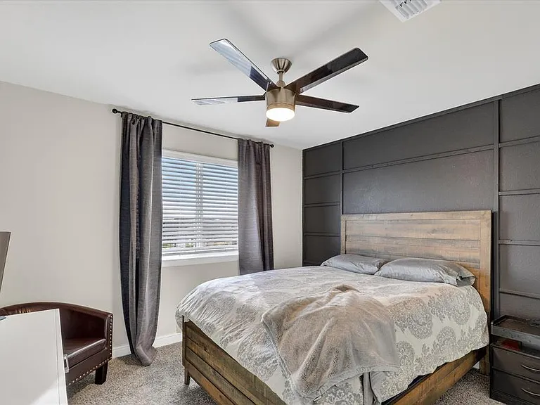Bedroom featuring a textured accent wall, ceiling fan with integrated lighting, and carpeted flooring