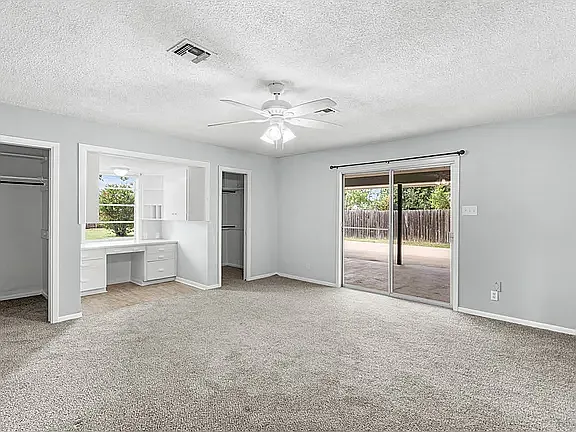 Huge Primary Bedroom with ceiling fan, 2 walk-in closets, desk area with cabinet storage overlooking the large backyard and sliding door opening to large patio and back yard. New gray carpet and fresh paint