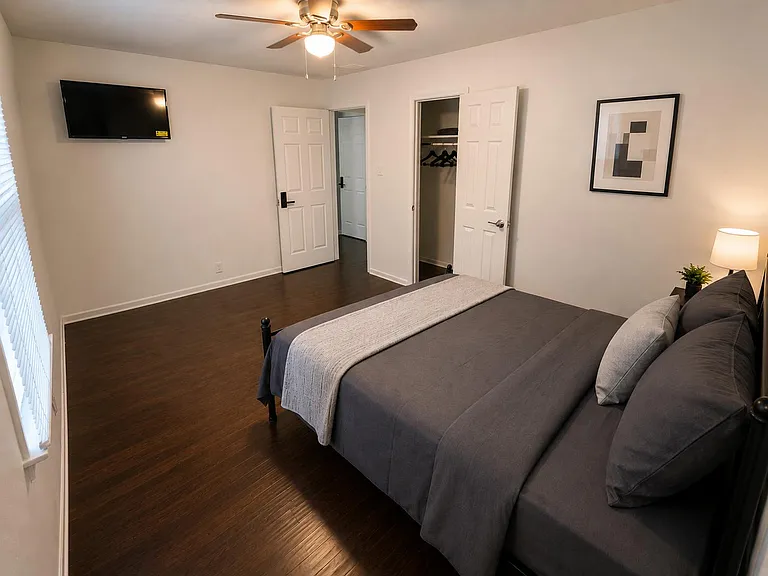 Furnished bedroom with hardwood floors, ceiling fan, wall-mounted TV, and a closet for convenient storage.