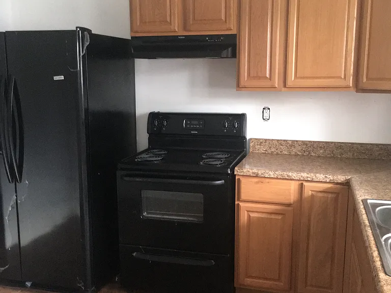 Kitchen with natural wood cabinets. Black refrigerator, oven and dishwasher.