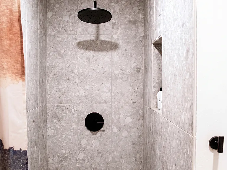Walk-in shower with terrazzo-style tile, matte black fixtures, and built-in niche.