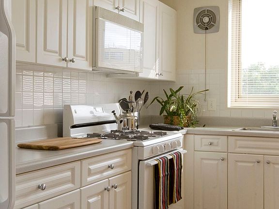 Kitchen with white cabinetry, white countertops, white appliances and tile backsplash