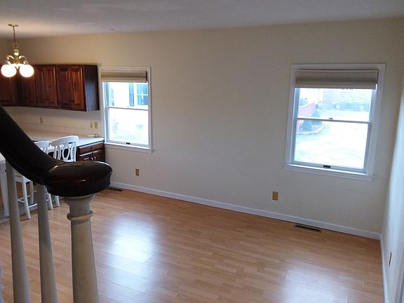 Living area viewed from the stairway landing. Entrance door (not seen) is to the right side. Kitchen on the left. Windows look out onto the next yard with driveway between.
